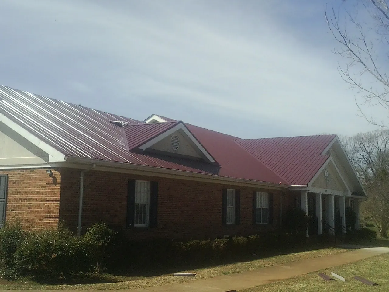 Red metal roof with gabled entries on a long brick building, from a Hail Damage Roof Repair job in Plantation