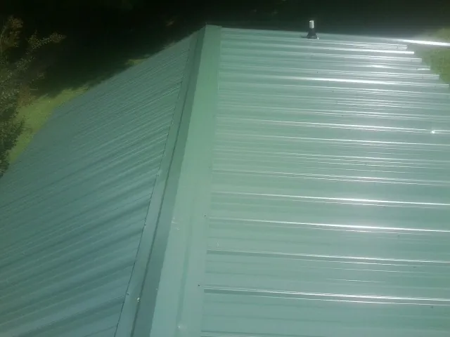 New green metal panels meeting at the ridge of a roof — Flat Roof Repair work by our crew in Plantation