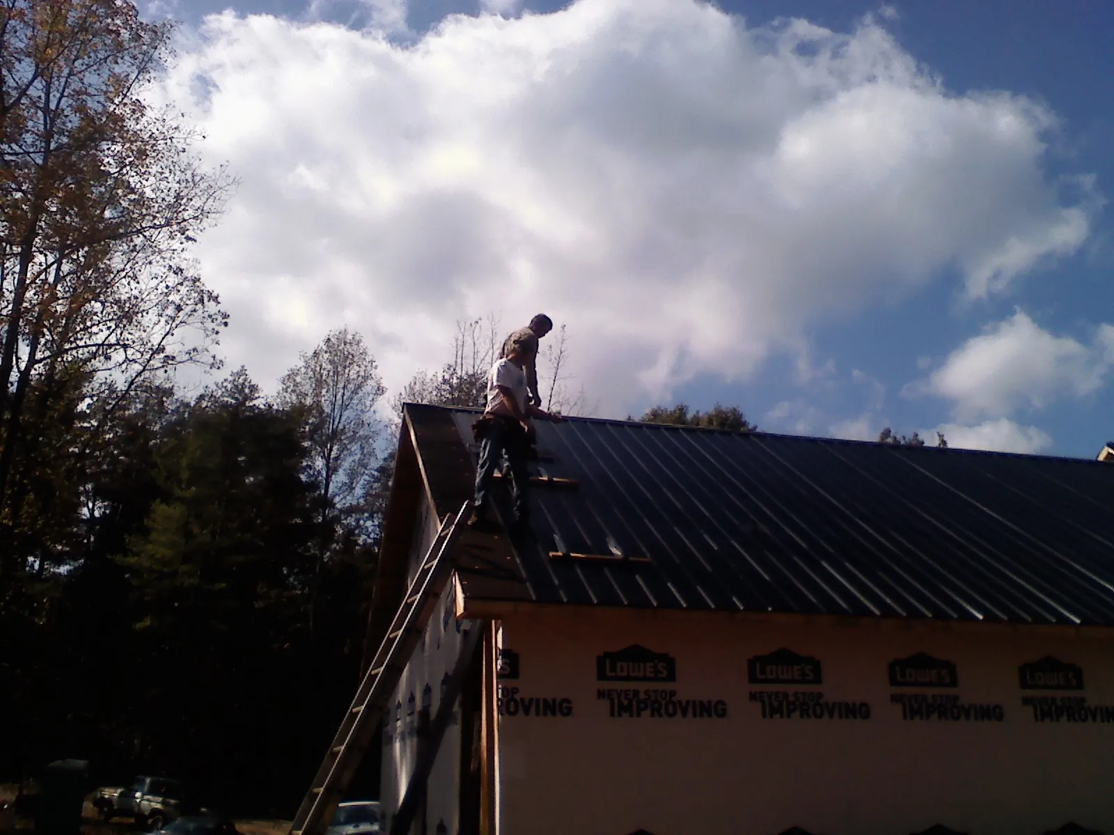 Roofer fastening dark metal panels high against a cloudy sky, from a Roof Inspection job in Plantation
