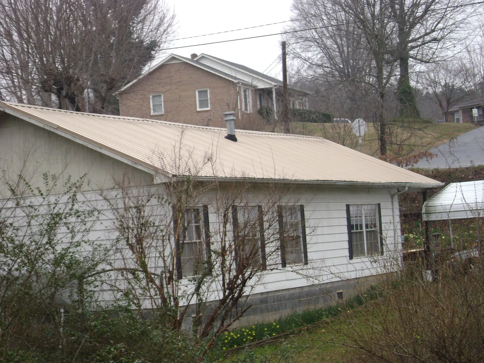 Tan metal roof on a white sided house set into a hillside — Commercial Roofing by Roofing Brothers in Plantation